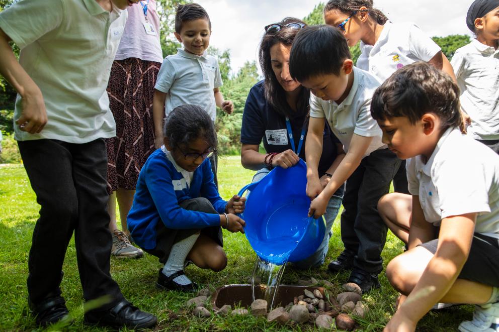 A group of children pouring water into a wildlife pond that they have built.